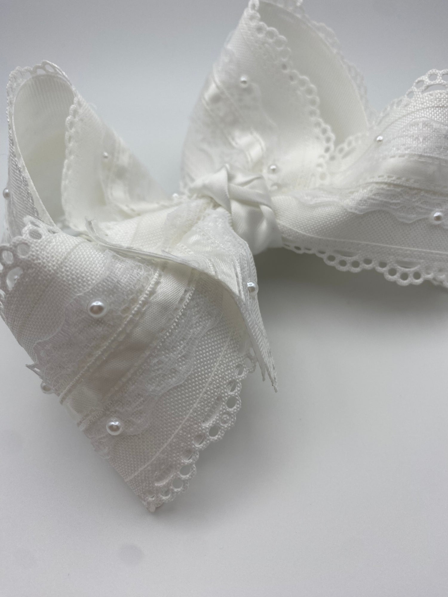 White lace bow with pearls layered on a white scalloped lace ribbon.